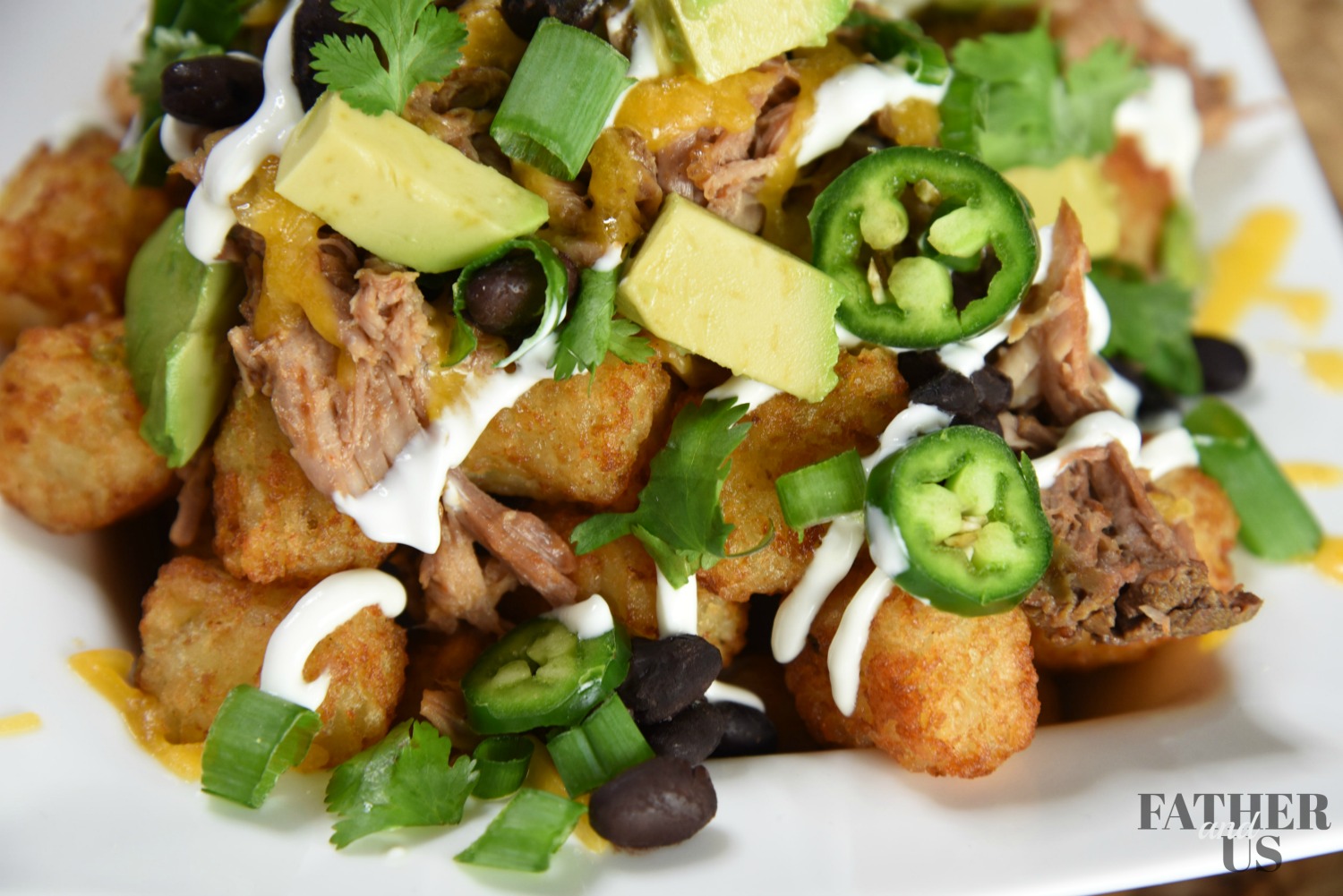 pulled pork totchos recipe in a white bowl with avocado, jalapenos and green onions.